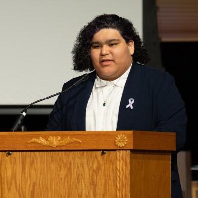 Headshot of Vienna Cavazos, LGBTQ+ Commission, speaking at an event behind a podium.