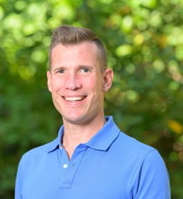 Headshot of Dwayne Bensing, LGBTQ+ Commissioner, smiling in a blue shirt.