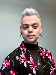 Headshot of Zachary Workman, LGBTQ+ Commissioner, smiling in a black shirt with pink flowers.